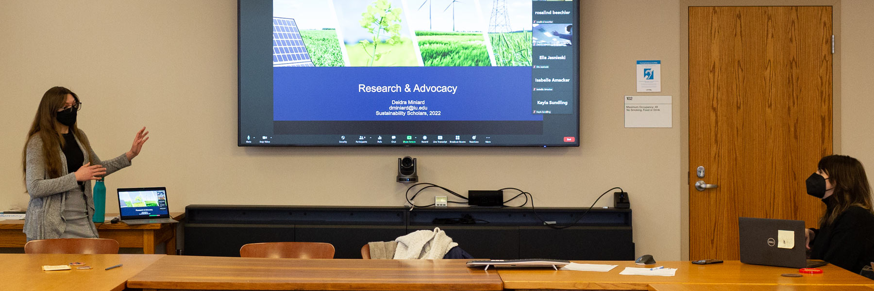 A young woman presents on a large screen at the Ostrom Workshop.